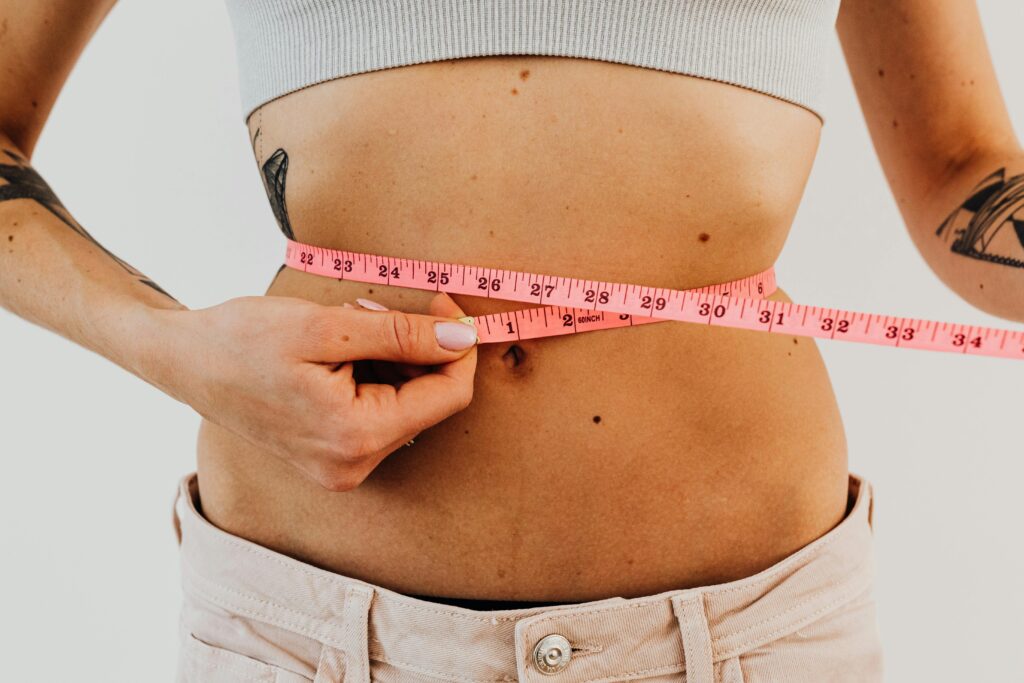pexels photo 5714347 5714347 A woman measuring her waist with a pink measuring tape, focusing on fitness and health.